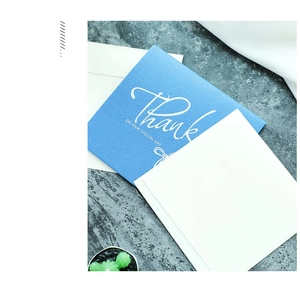 Close-up of blue square Thank You card with white envelope on a grey textured surface