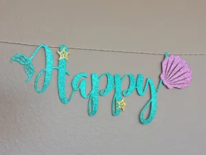 Detail of glitter Happy Birthday banner featuring mermaid tail and purple shell accents