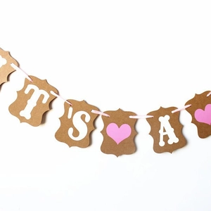 Baby shower party banner with It's A text and pink heart on kraft paper card