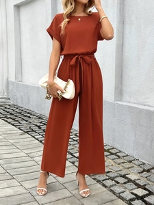 Detail of rust orange short sleeve jumpsuit featuring a tied waist and wide leg cut