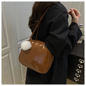 Brown glossy shoulder bag with a white plush pompom charm shown on a model