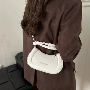 White crescent underarm bag with twisted handle and gold logo worn by a model