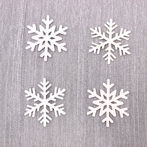Set of four white 3D snowflake table decorations for Christmas on a textured grey surface