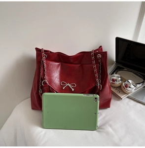 Detail of red faux leather tote with metal bow buckle and chain, showing spacious capacity