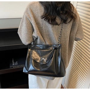 Detail of black glossy shoulder bag with silver bow and metal chain strap on model
