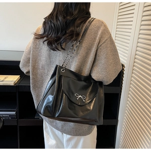Detail of black leather tote bag with silver bow accent and chain shoulder strap