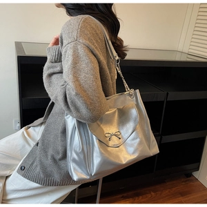 Detail of silver tote bag with metal bow accent and chain strap on female model