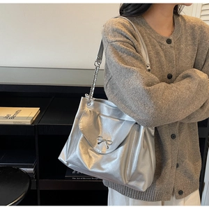 Chic metallic silver crossbody bag with metal bow detail shown on a female model