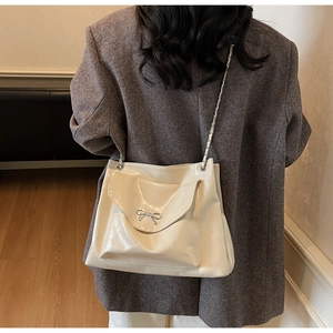 Detail of a chic beige glossy leather shoulder bag with a silver metallic bow decoration