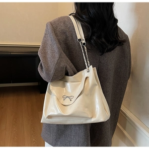 Close-up of cream shoulder bag featuring glossy finish and elegant metal bow detail