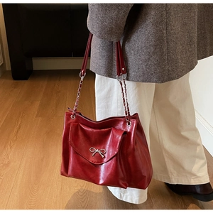 Detail of dark red glossy leather tote with elegant silver bow buckle and chain strap