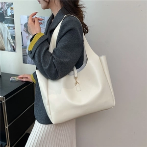 Minimalist cream leather tote bag with gold hardware shown as a shoulder bag on a model