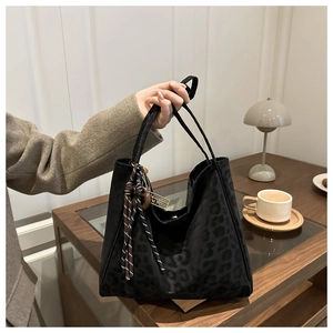 Detail of dark leopard print tote bag with contrast tassel and metal charm accessory
