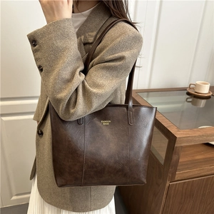 Fashionable dark brown leather tote bag with gold lettering shown on shoulder with a model