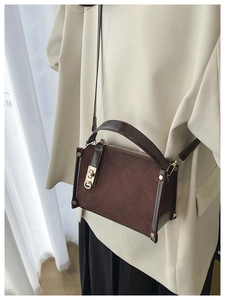 Detail of dark brown quilted crossbody bag with gold twist lock on a stylish outfit