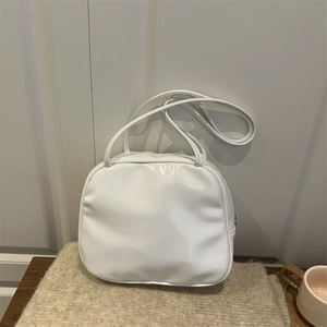 Glossy white minimalist pillow bag with shoulder straps on soft knit background