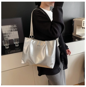 Silver metallic tote bag with bow detail and metal rings shown on a shoulder