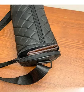 Close-up of black quilted nylon cylinder bag featuring a side zipper pocket and strap