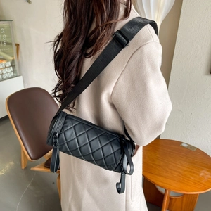 Close-up of a black quilted barrel crossbody bag with an adjustable wide shoulder strap
