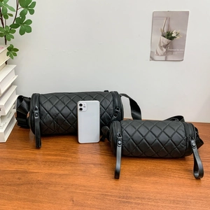 Detail of two black quilted barrel bags in different sizes on a wooden desk with plants