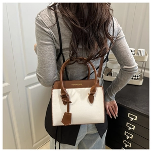 Close-up of white and brown contrast leather handbag with round handle and gold lettering