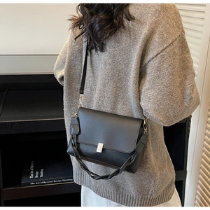 Detail of black leather crossbody bag with silver buckle and braided handle on model