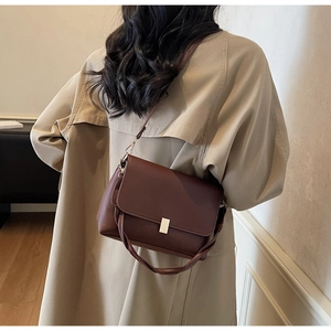 Detail of a dark brown crossbody bag featuring golden buckle and woven handle on trench coat