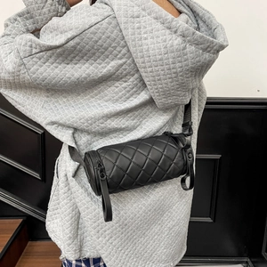 Quilted black cylinder crossbody bag shown on model with minimalist modern urban aesthetic
