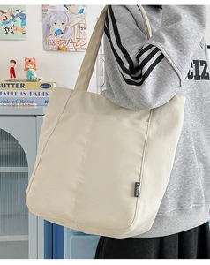 Detail der beigen Canvas-Tragetasche mit schwarzem FASHION-Label und vertikalen Nähten
