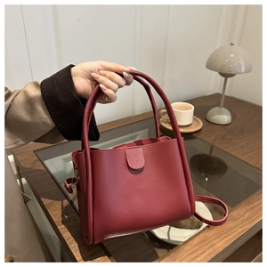 Détail d'un sac à main en cuir bordeaux avec doubles poignées et une bandoulière amovible