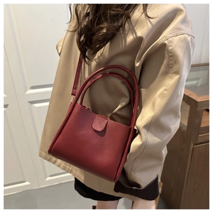 Mannequin portant un sac seau en cuir bordeaux mat avec bandoulière croisée chic