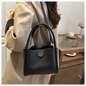 Detail of a black matte bucket bag styled with a beige trench coat for a casual look