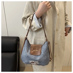 Close-up of blue denim shoulder bag featuring brown leather trim and golden logo detail