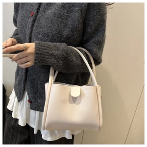 Side view of cream leather bucket bag with magnetic flap worn by a model in a minimal style