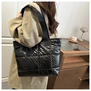 Detailed view of black quilted puffer tote bag worn on shoulder in a cozy cafe setting
