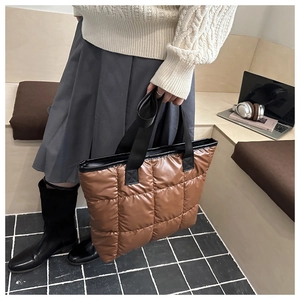 Close-up of brown quilted puffer tote bag with black strap held by model in knit sweater