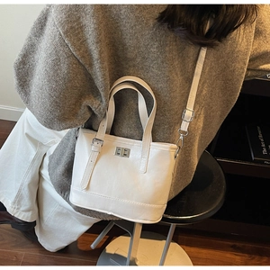 Détail du sac seau en cuir blanc avec fermoir rotatif argenté sur une tenue tricot