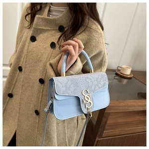 Detail showing the light blue snakeskin texture and gold S-shaped buckle on the handbag