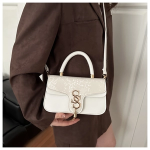 Detail of white crocodile texture on small square bag with gold SS logo and metal tassel