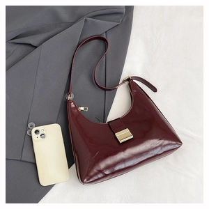 Detail of burgundy semi-moon handbag with glossy finish and gold metal buckle