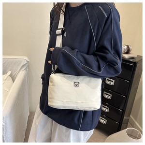 Detailaufnahme der weißen Canvas-Umhängetasche mit Bärenstickerei und breitem Schultergurt