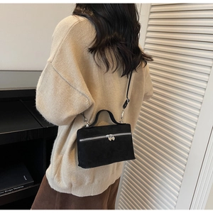 Détail d'un sac en daim noir avec zips en cœur porté sur un pull en maille beige clair