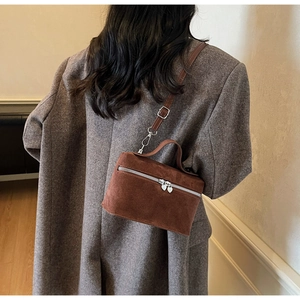 Detail der karamellfarbenen Wildleder-Box-Tasche mit Herz-Reißverschluss am grauen Blazer