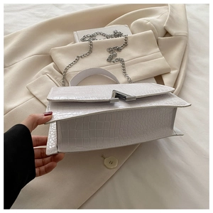 Detail of white crocodile embossed leather bag with silver V-shaped metal lock and chain strap