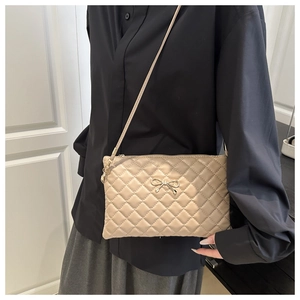 Dettaglio della trama trapuntata beige e del fiocco in metallo dorato sulla borsa