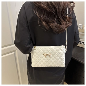 Detail of white quilted crossbody bag featuring a gold bow accent and zip closure