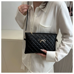 Detail of black quilted crossbody bag featuring a golden bow metal clasp and slim strap
