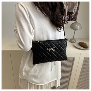 Detail of black quilted leather shoulder bag with gold bow clasp and elegant chain strap