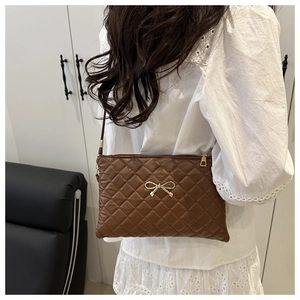 Detail of brown quilted crossbody bag with gold bow clasp worn by a model