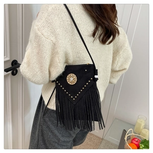 Model wearing a black bohemian crossbody bag with long tassels and gold rivet details
